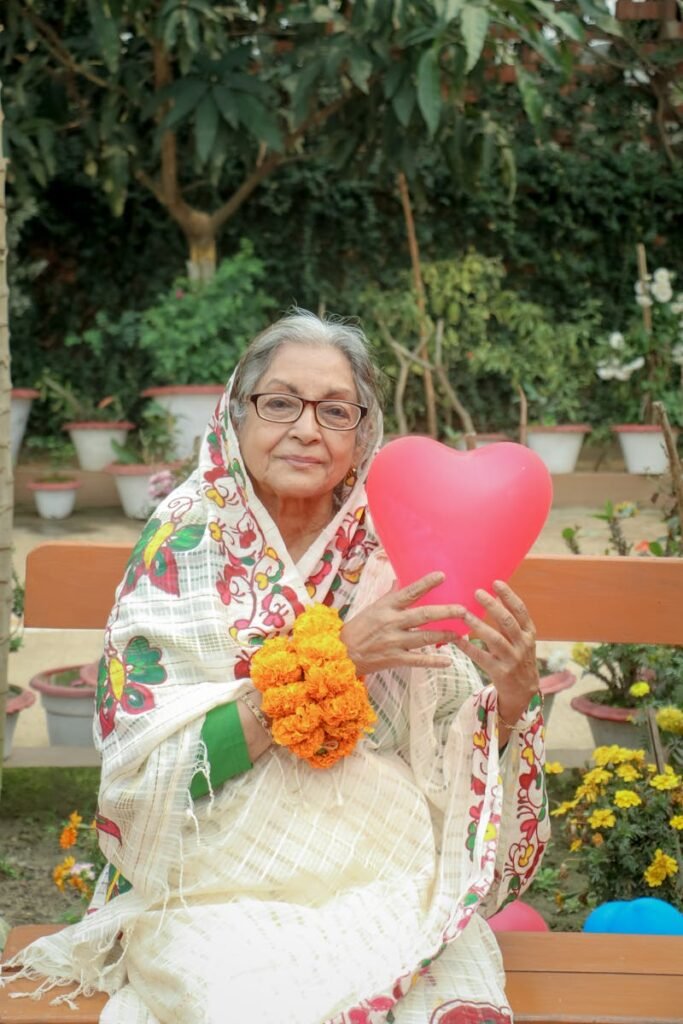 Elderly woman in traditional clothing with heart balloon, sitting outdoors.